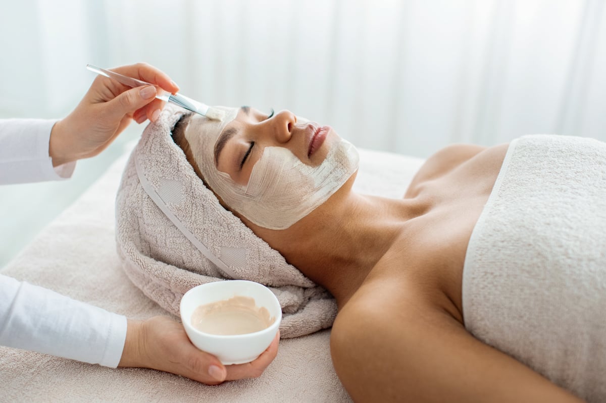 Esteticista profesional aplicando mascarilla facial a mujer en spa de lujo, ambiente relajado con luz suave